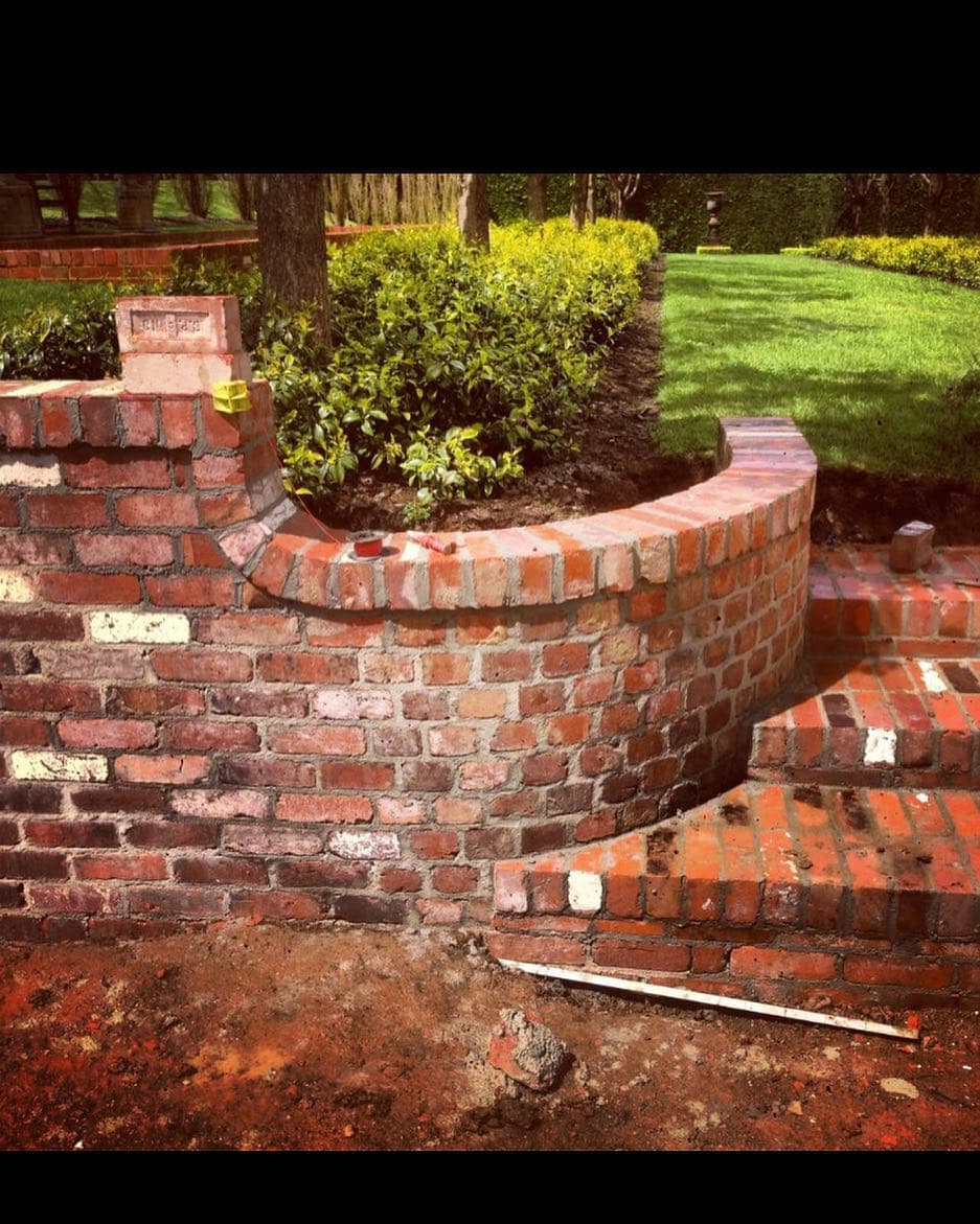 Double-tier free-hand curved red-brick planter with cascading courses, every brick cut and set by eye.