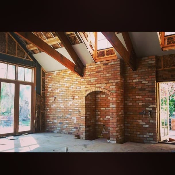 Interior with hand-laid red-brick archway and feature wall under exposed timber rafters, recent work