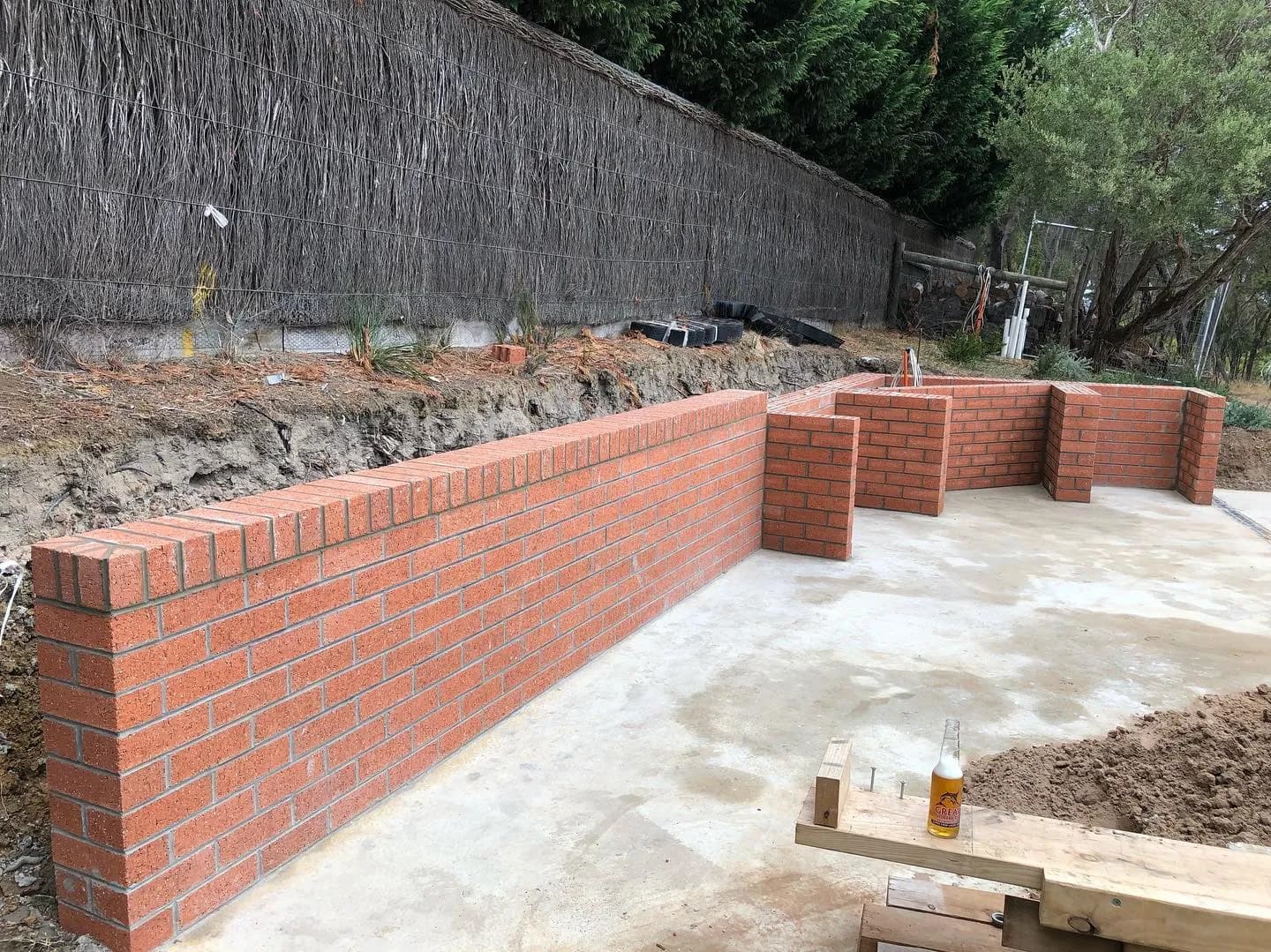 Crisp red-brick L-shaped boundary wall with thatched fence behind